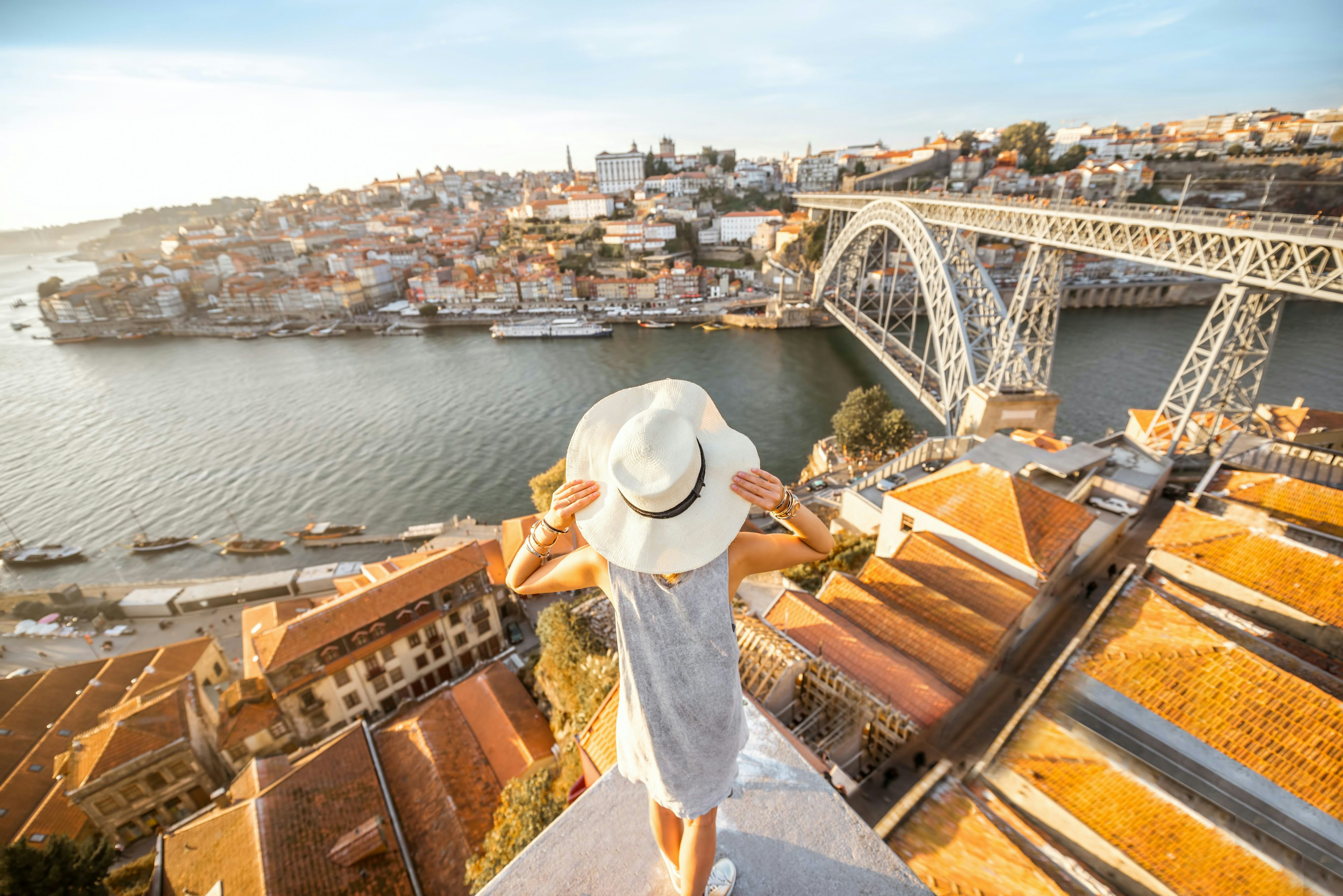 A picture of a woman holding her hat whilst looking at a bridge over a river in Porto