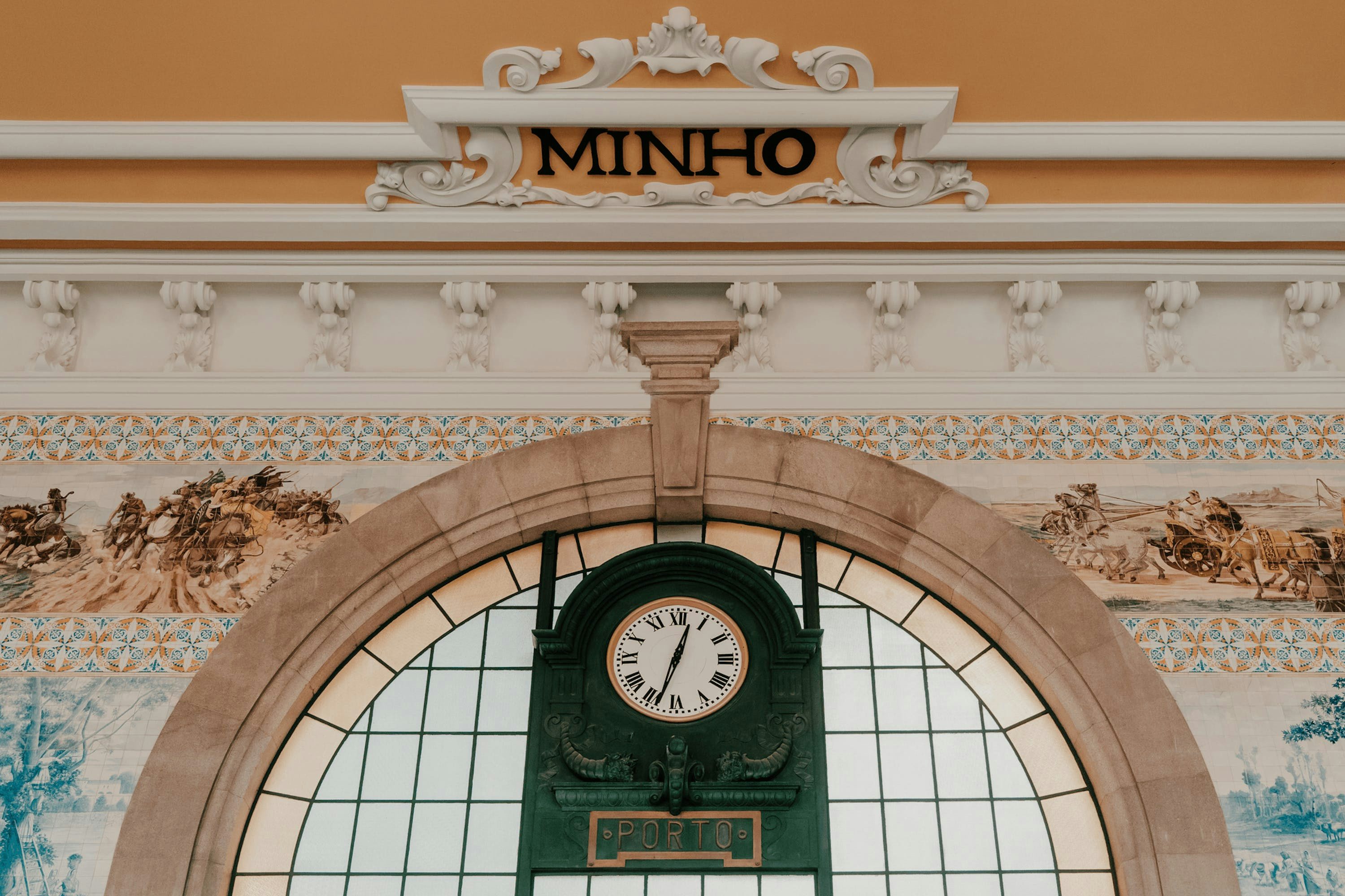 Relógio ornamentado montado em uma parede decorada com azulejos azuis e brancos na Estação São Bento no Porto.