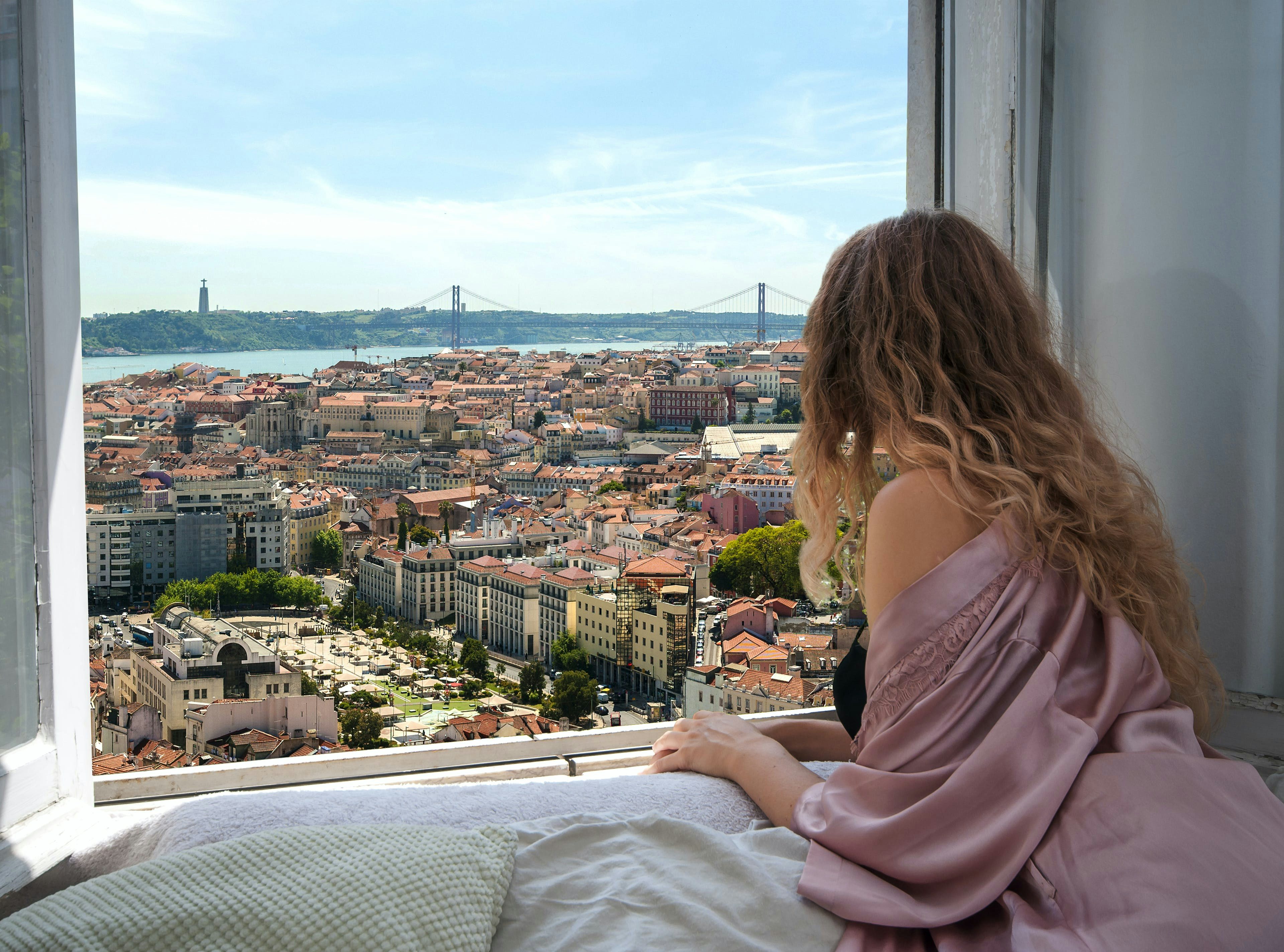 Mulher olhando pela janela para a cidade de Lisboa