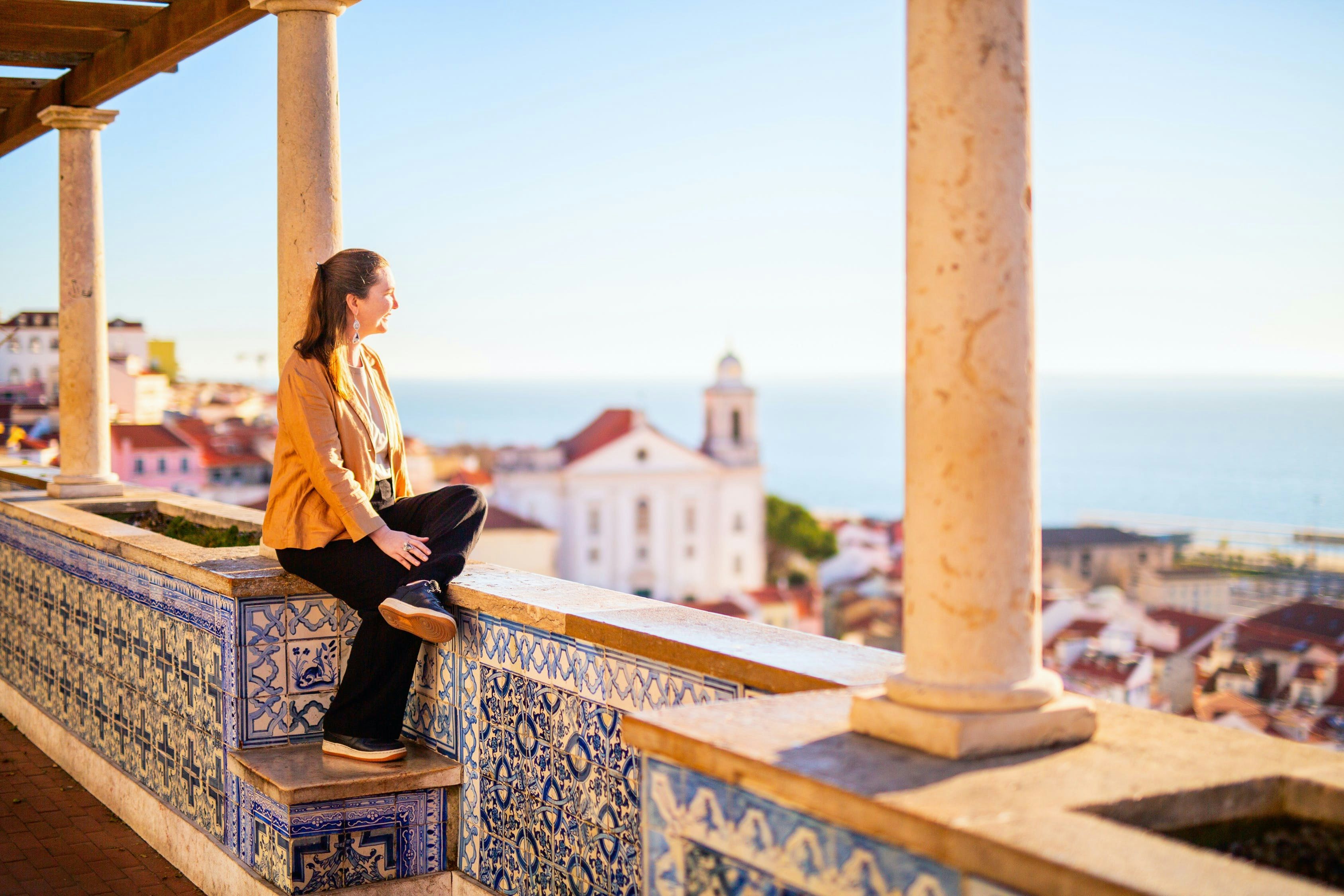 Uma mulher sentada em um mirante olhando para uma cidade em Portugal