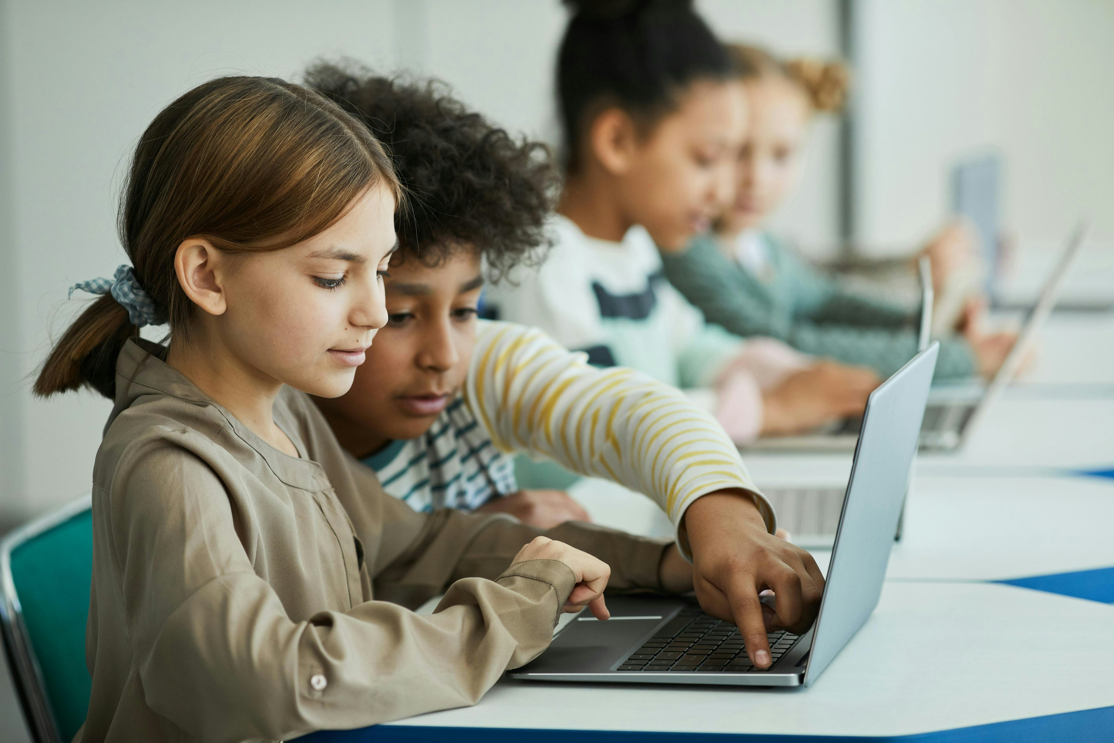 Crianças em uma mesa estudando com laptops