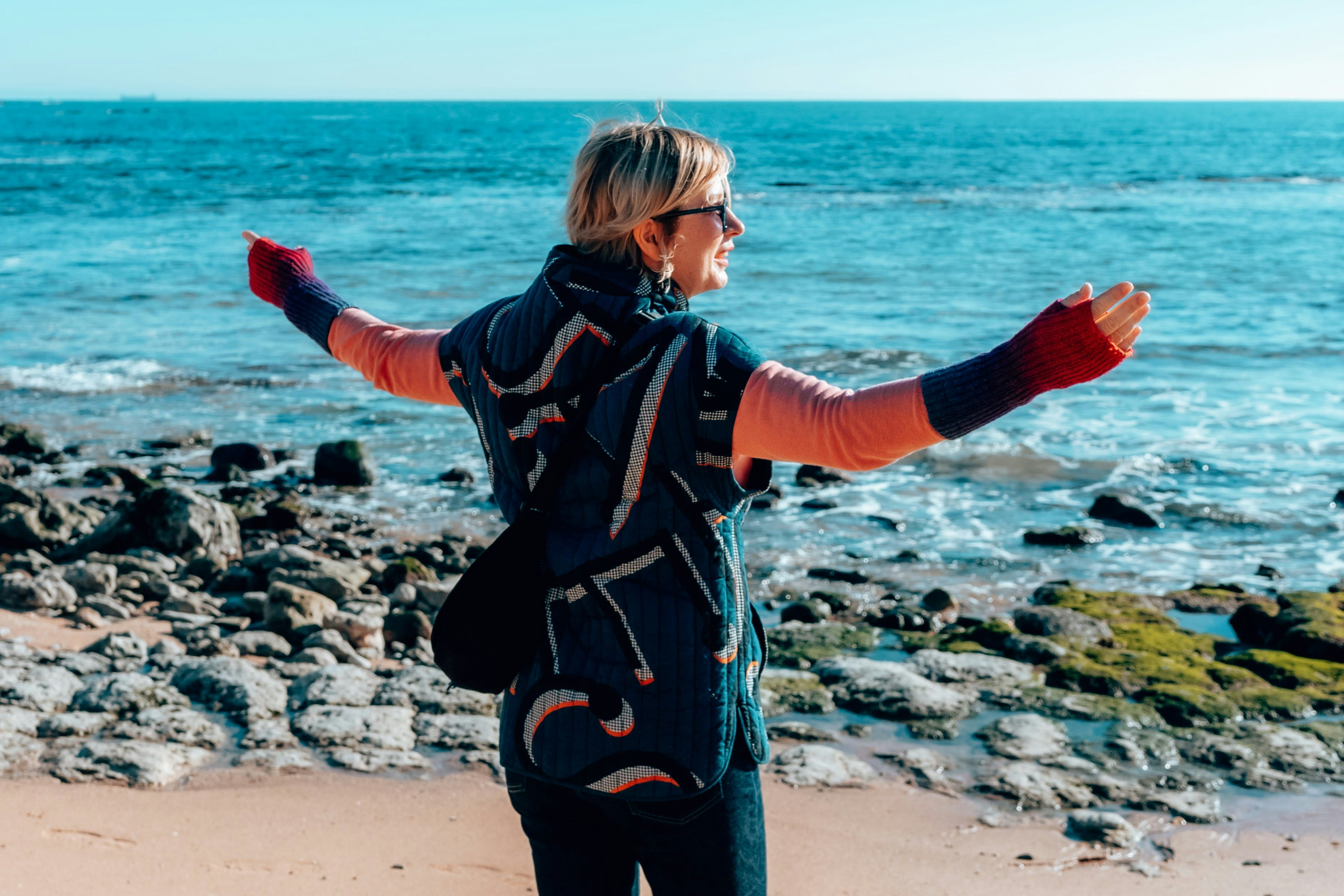 Imagem de uma mulher de costas para a câmara, com os braços bem abertos, de frente para o Oceano Atlântico em Portugal