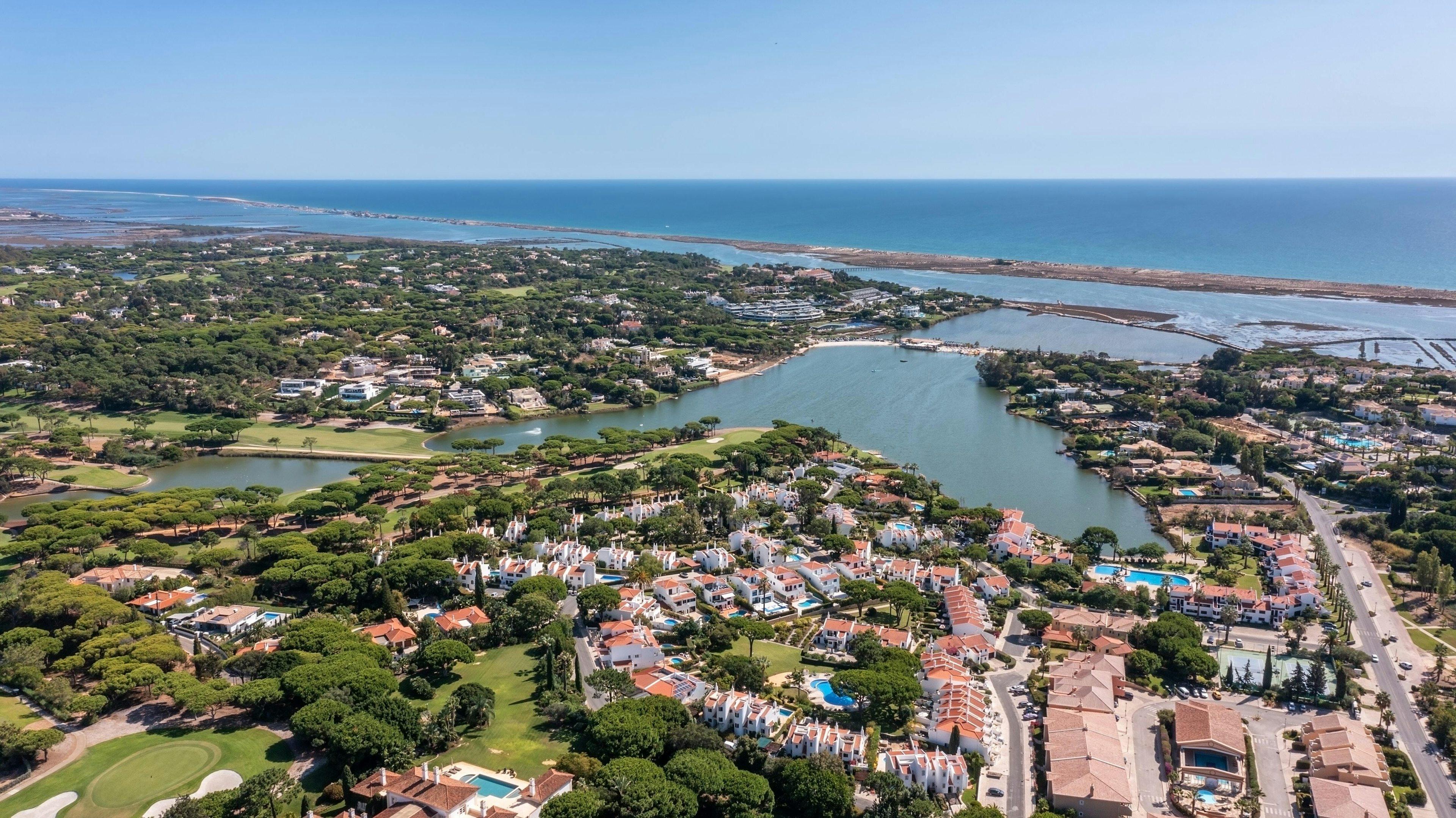 Vista panorâmica da costa algarvia apresentando cidades movimentadas justapostas ao oceano tranquilo.