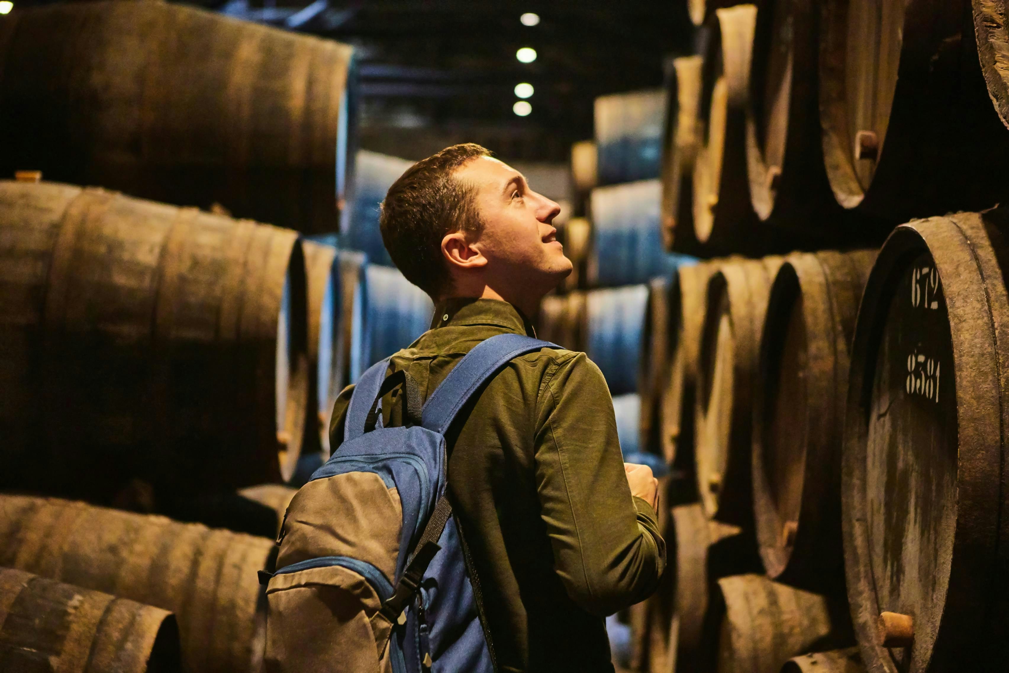 A photo of a man looking at barrels of wine in a cellar