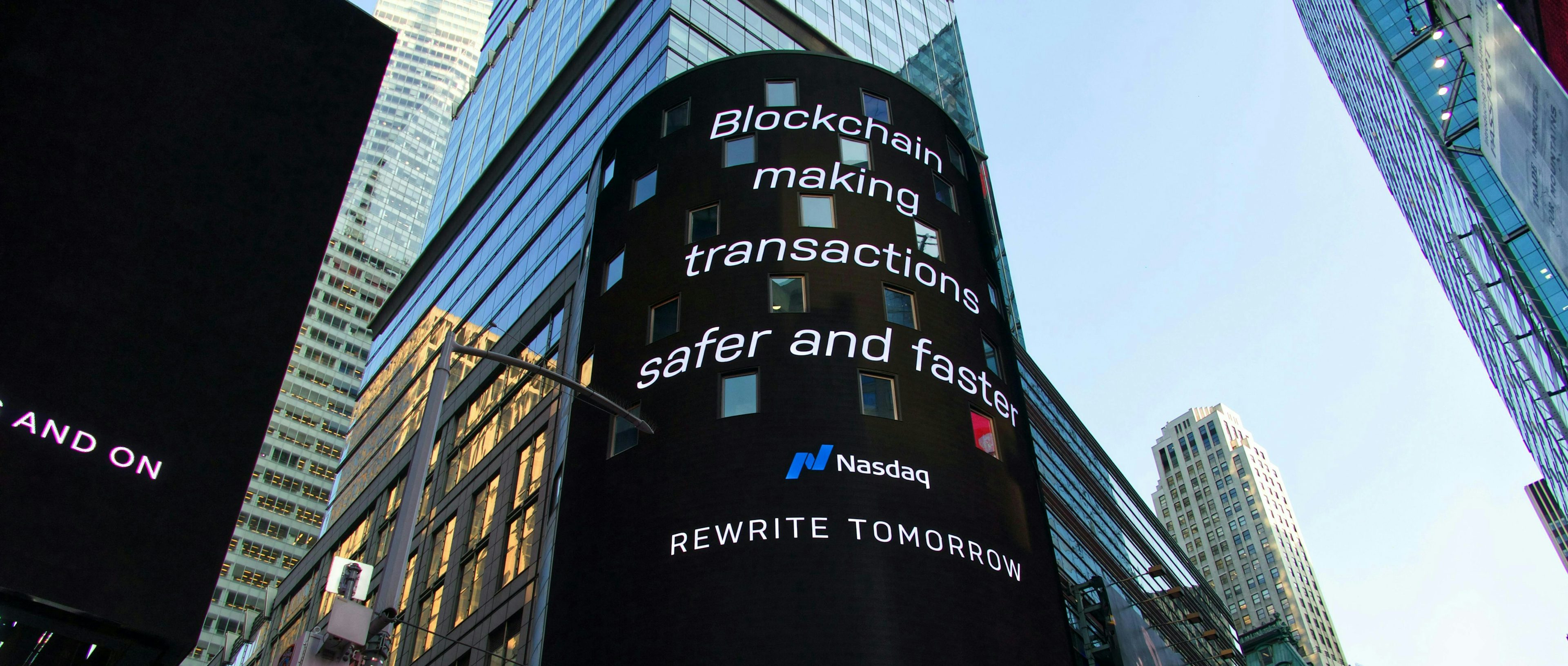 An image showcasing a digital advertisement by Nasdaq displayed on the facade of a tall building. The ad prominently features the text "blockchain making transactions safer and faster," highlighting the benefits of blockchain technology in financial transactions.