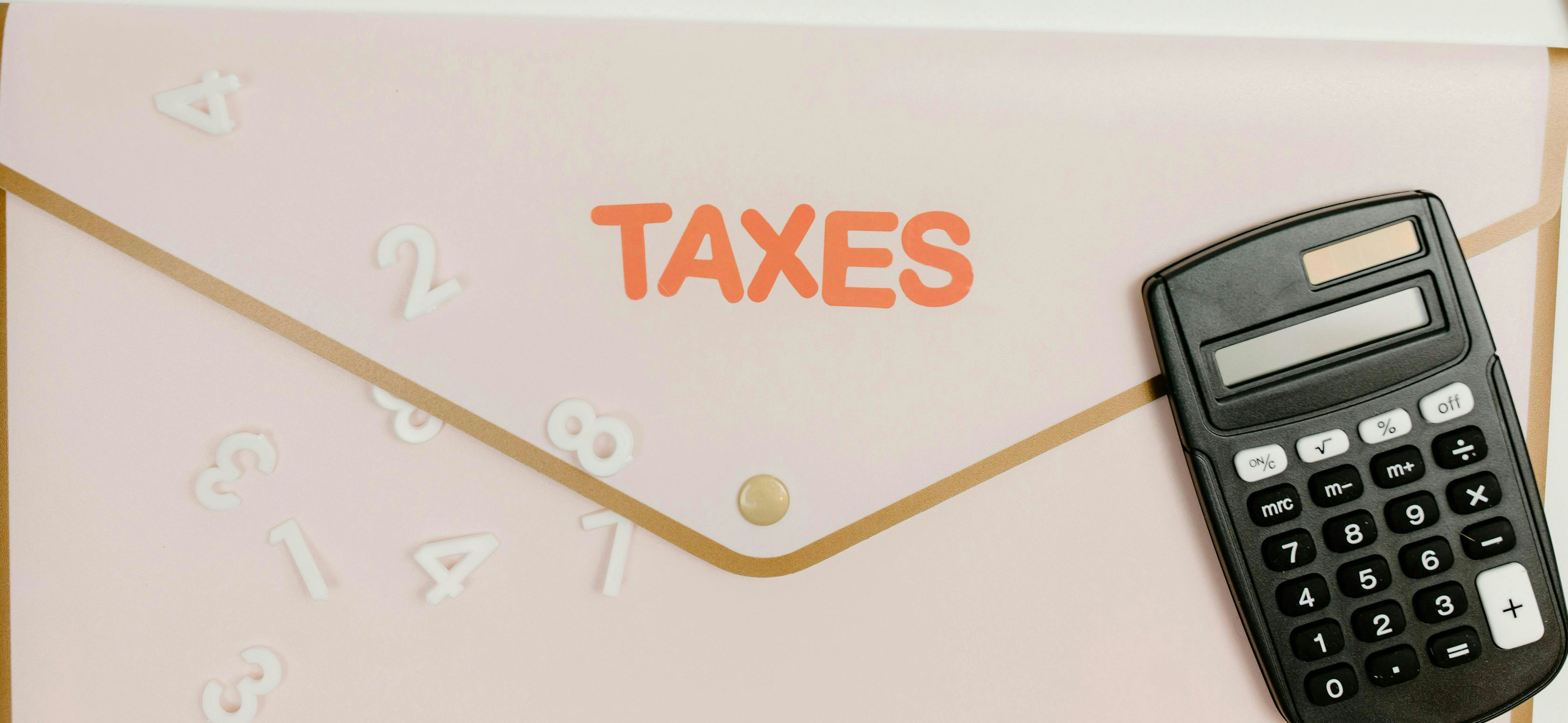Salmon-colored envelope with golden trimmings, labeled 'taxes' in orange letters, with a black calculator placed on the right bottom corner of it.