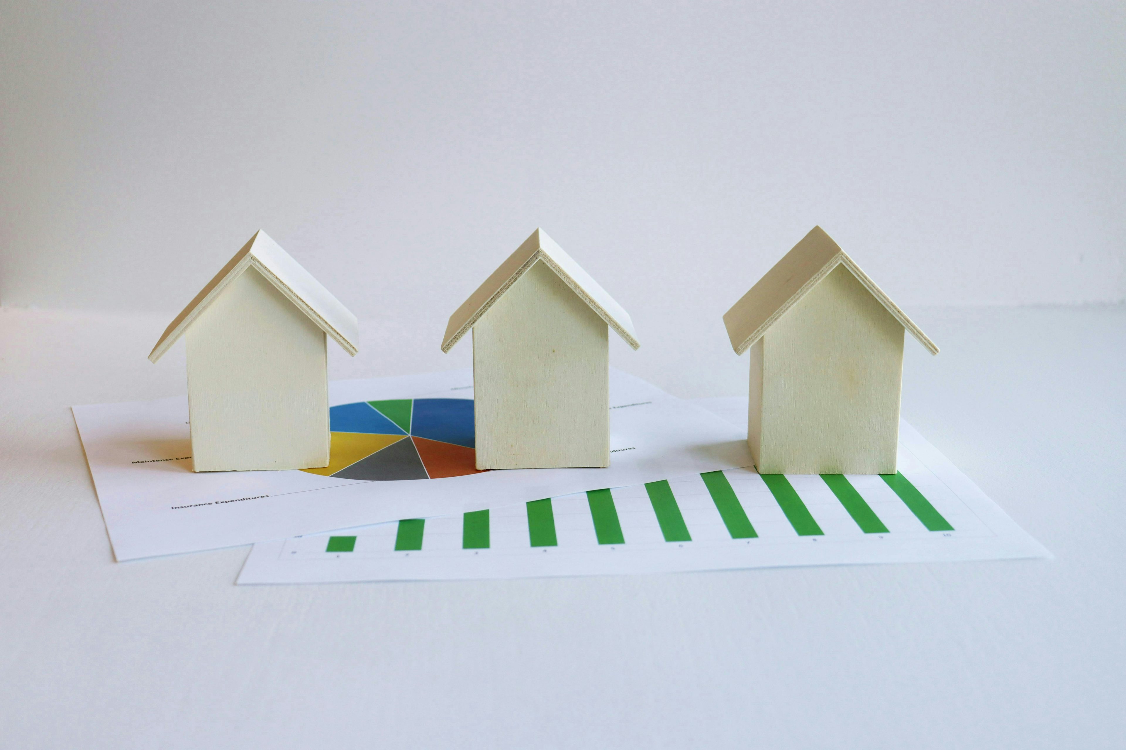 Three plywood model houses placed on top of two sheets of paper, one displaying a pie chart and the other showing a bar graph.