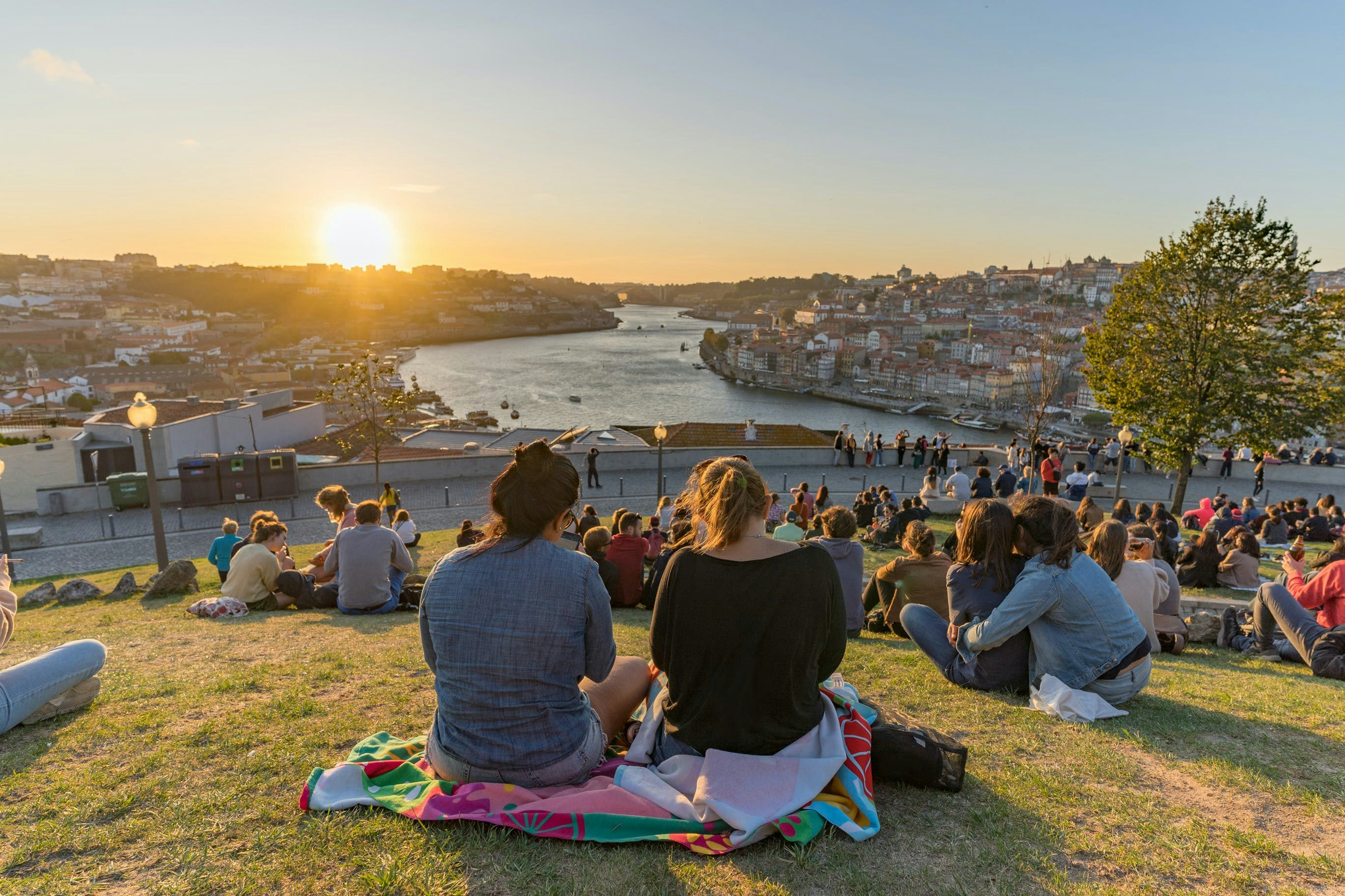 An image of people on rugs on the grass overlooking a city and river